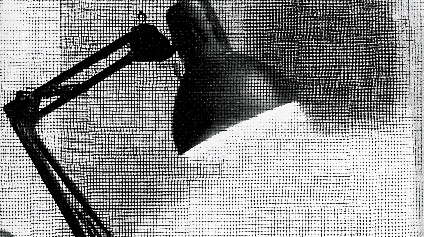 An Anglepoise lamp in silhouette, its jointed arm angled over a lit desk.